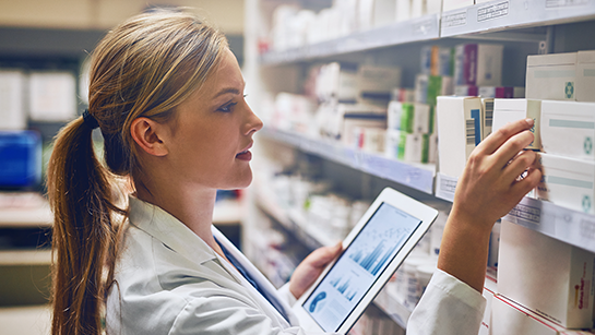 Apothekerin, die während ihrer Arbeit in einem Regal ihr Tablet benutzt.