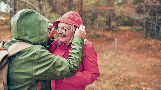 Beratungsaktion Erkältung: Ein Pärchen lacht gemeinsam bei Regen im Wald.