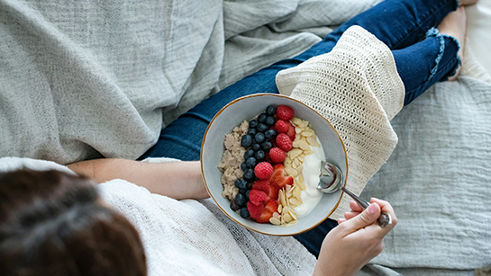 Eine Frau sitzt mit einer Joghurtbowl auf dem Schoß.