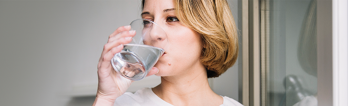 Frau trinkt Wasser in der Nähe des Fensters