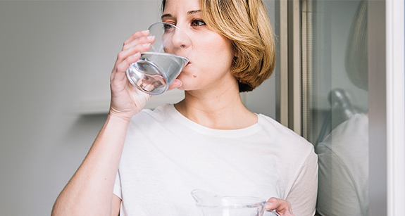 Frau trinkt Wasser in der Nähe des Fensters