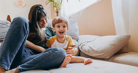Titelbild Kategorie Gesundheitstipps Gesundheit: Eine Mutter sitzt mit Ihrem Kind auf dem Sofa und lacht.