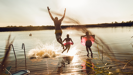 Freunde, die einen Sommertag genießen, indem sie vom Steg in den See springen.