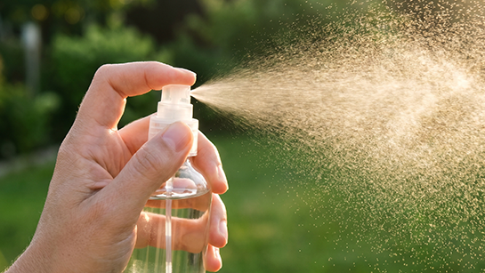 Nahaufnahme einer Hand, die mit einer Sprühflasche Erfrischungsspray in die Sonne sprüht.