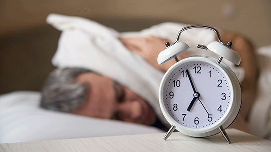 Man liegt im Bett und schaltet einen Wecker am Morgen ab